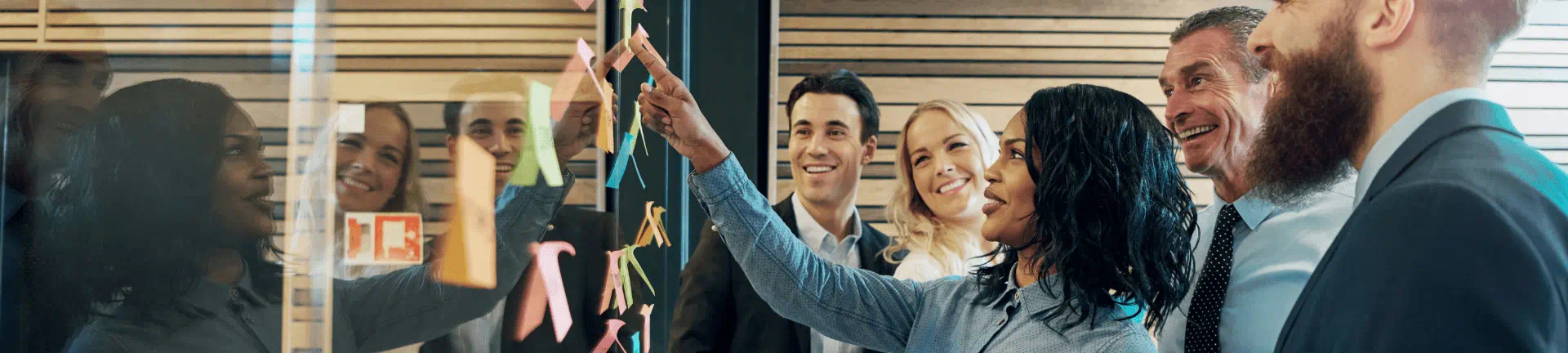 A group of diverse professionals engages in problem-solving, analyzing sticky notes on a wall in an office setting. A group of diverse professionals engages in problem-solving, analyzing sticky notes on a wall in an office setting.