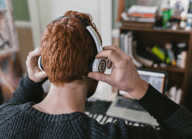 The back of a man’s head as he puts on headphones in his cozy home office. 