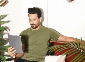 A young man relaxing on a couch, casually holding a tablet and looking at its screen.
