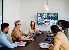 A team of colleagues collaborates in a modern office room, gathered around a large table with a big screen displaying a conference call. A team of colleagues collaborates in a modern office room, gathered around a large table with a big screen displaying a conference call.
