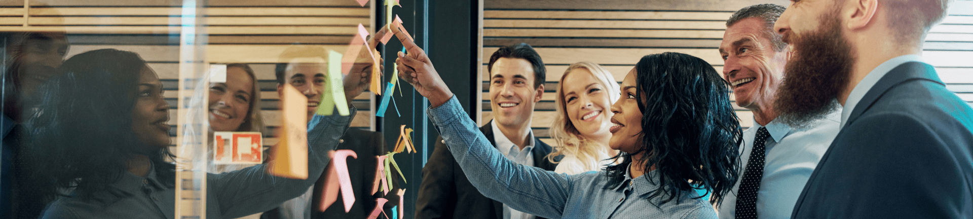 A group of diverse professionals engages in problem-solving, analyzing sticky notes on a wall in an office setting.
