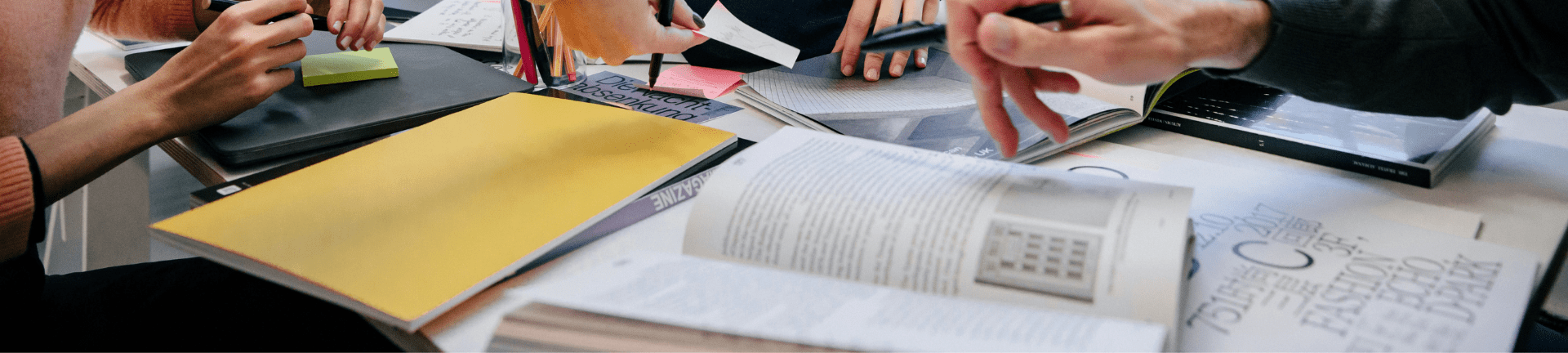 Team members focused on tasks at a desk, equipped with books and pens, discussing managed service and recruitment outsourcing information.