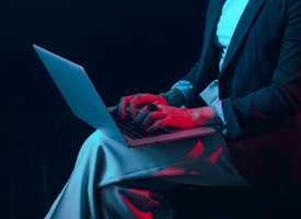 A modern woman is sitting in a dimly lit space, intently typing on a laptop. The soft, dark lighting creates a moody atmosphere.