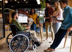 A man in a wheelchair engaging in a productive discussion with his colleagues in a cozy office setting. A man in a wheelchair engaging in a productive discussion with his colleagues in a cozy office setting.
