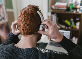 The back of a man’s head as he puts on headphones in his cozy home office.