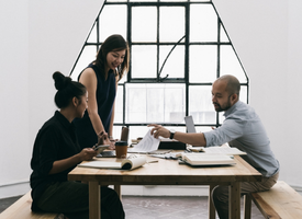 Coworkers seated around a bench and table in a bright, white office, actively discussing a project. The scene is clean and modern, with natural light enhancing the workspace. Coworkers seated around a bench and table in a bright, white office, actively discussing a project. The scene is clean and modern, with natural light enhancing the workspace.